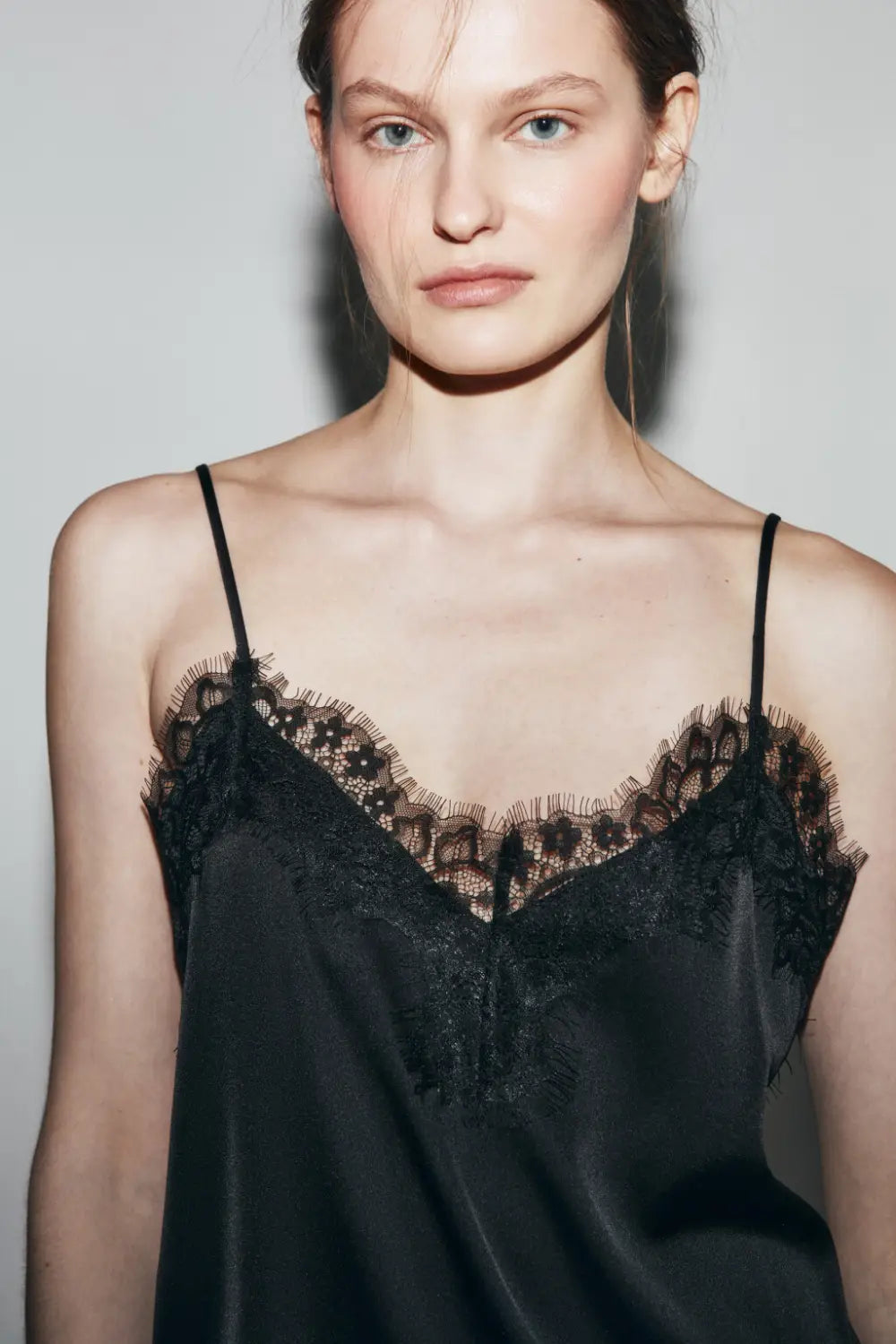 Schwarzes Satin-Camisole-Top mit zartem Spitzenbesatz entlang des Ausschnitts und der Träger, entworfen für elegantes Tragen.
