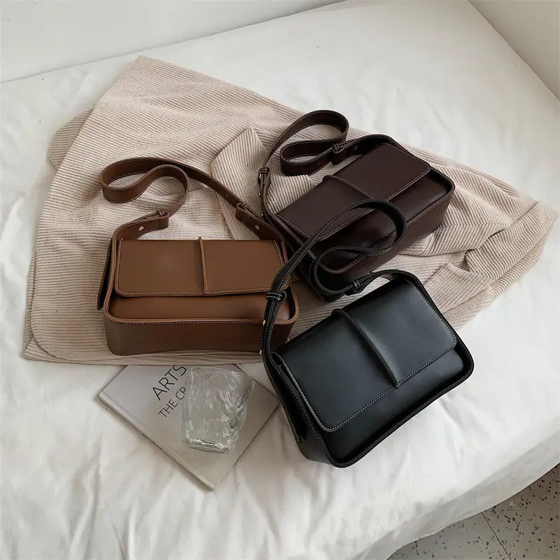 Three rectangular crossbody bags in brown and black faux leather with stitched flap closures for minimalist shoulder purse use.