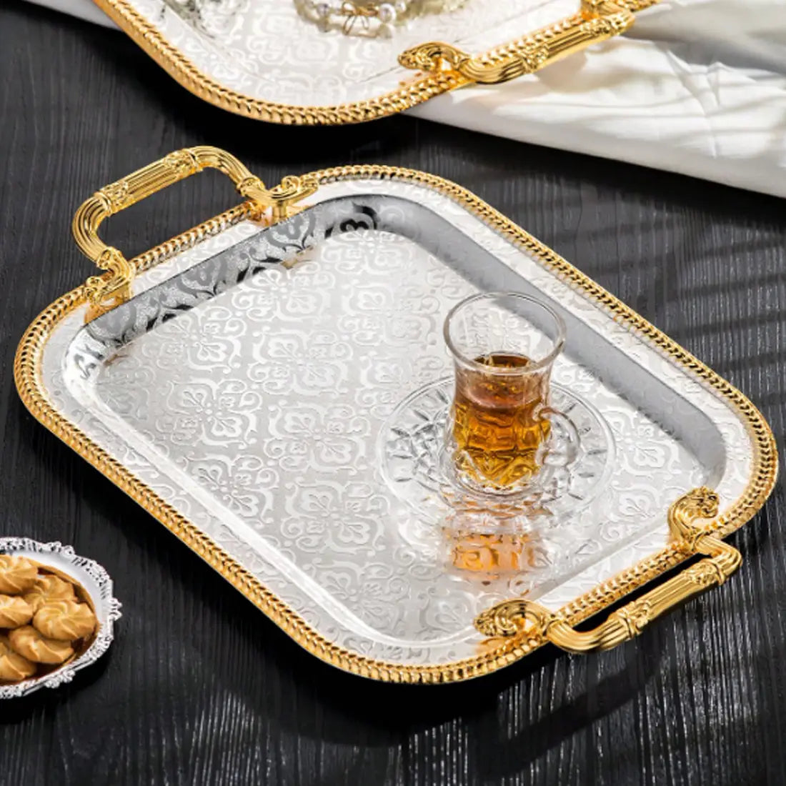 Luxury rectangle serving tray with silver body, ornate gold handles, embossed floral patterns, holding a glass of tea.