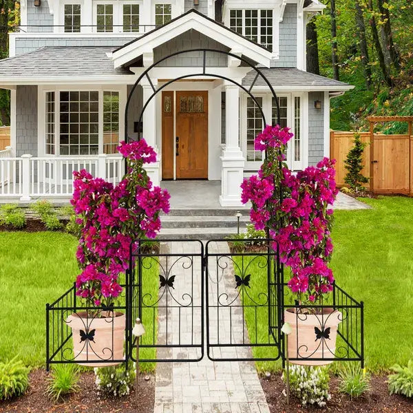 geschmiedeter schwarzer Metall-Gartenbogen aus Eisen mit Tor, Schmetterlingsrankengitter, Laube, flankiert von lebhaft blühenden violetten Pflanzen in Terrakotta-Töpfen