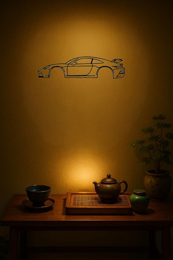 Eine minimalistische schwarzmetallische Line-Art-Silhouette eines Porsche 911 Sportwagens als Aufkleber, an einer warm getönten Wand über einem Holztisch mit Teegeschirr präsentiert.