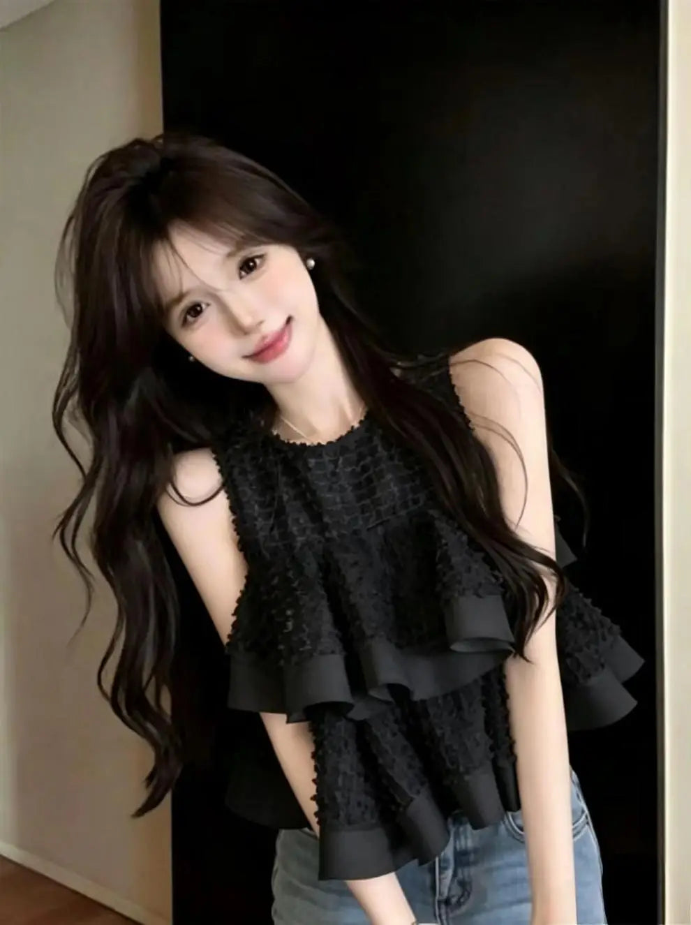 Blusa negra sin mangas con volante fruncido que presenta tejido con textura y volantes en capas para un look elegante y estilizado.
