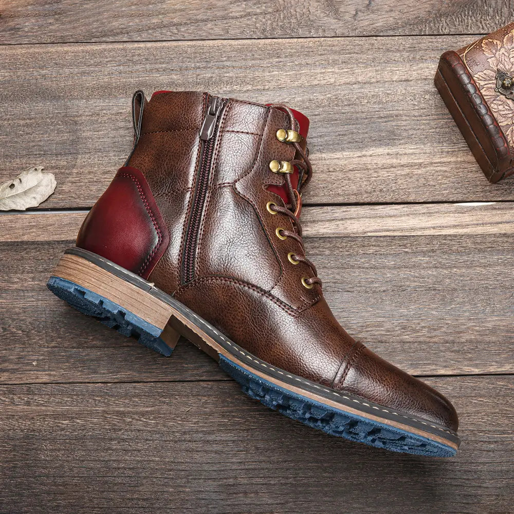 Brown leather ankle boots with a contrasting red panel on the side, brass eyelets, gold-toned zipper, and a blue rubber sole.
