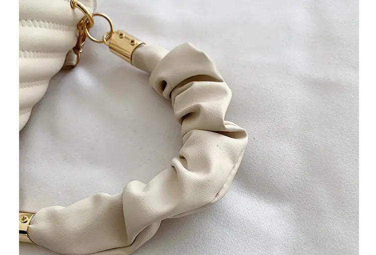 Cream-colored ruched leather strap with gold-tone metal hardware on a quilted heart clasp crossbody bag with ruched handle.