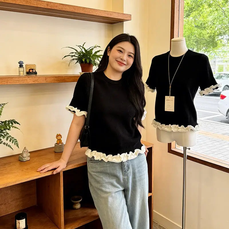 Black short-sleeved knit top with delicate white ruffled trim at the cuffs and hem designed as a colorblock ruffled short sleeve knit top.