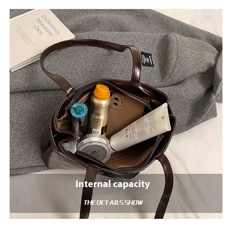 Brown faux leather buckle shoulder tote bag with zipper closure and visible internal compartments featuring a bow charm.