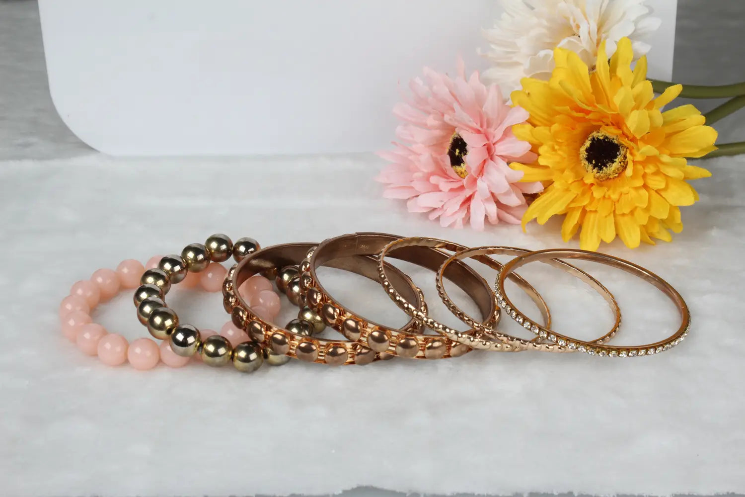 A collection of rose gold and pink beaded rhinestone bangle bracelets with metallic accents arranged neatly on a white surface.