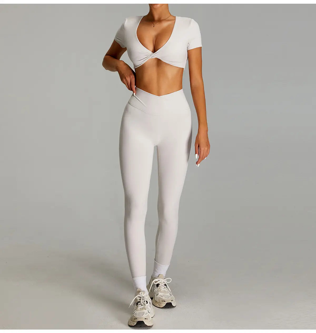 Haut court blanc à encolure plongeante en V et manches courtes, associé à des leggings de sport assortis taille haute effet nu à séchage rapide pour le fitness.