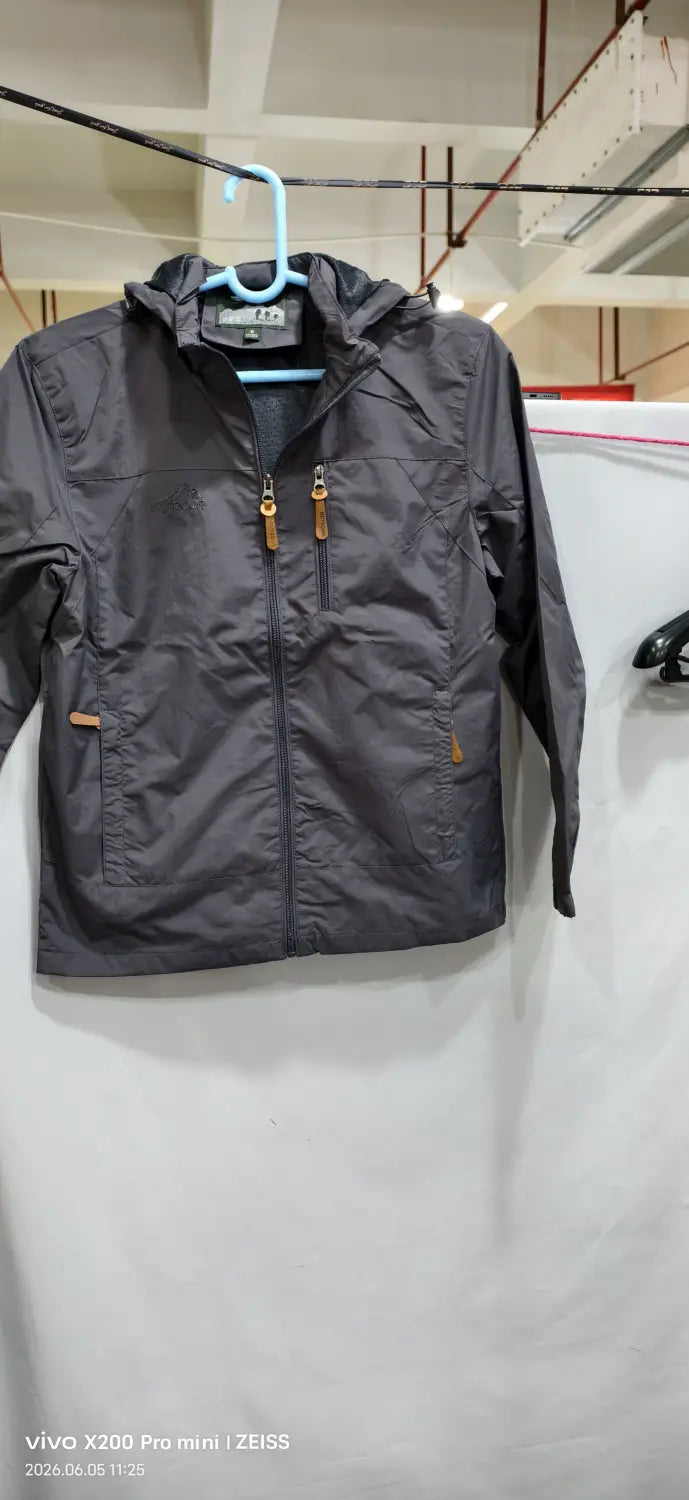 Chaqueta de senderismo con capucha impermeable color gris oscuro, con cierre frontal mediante cremallera y bolsillos laterales, con cremalleras de color camel.