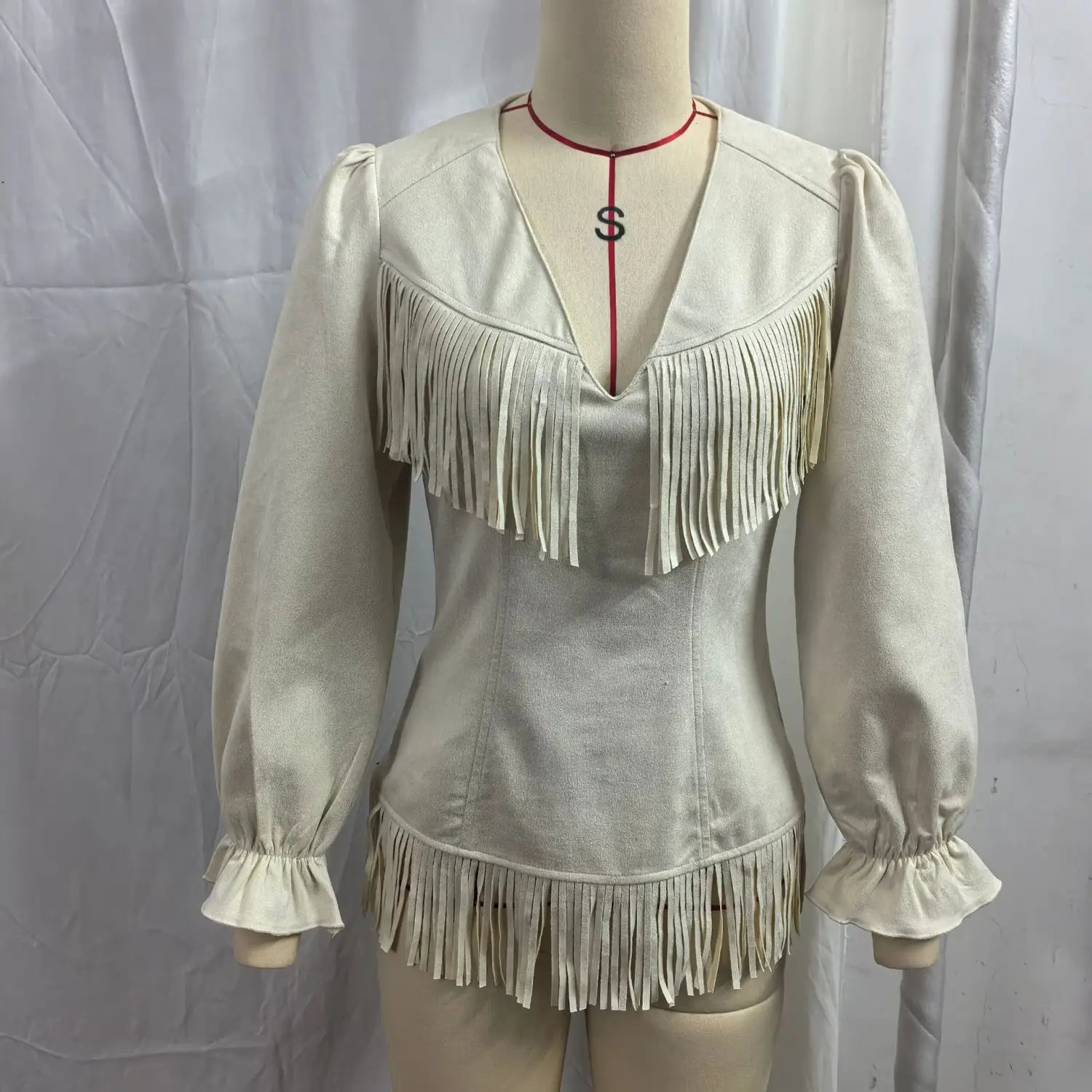 Beige fringe suede v neck jacket featuring cream-colored suede with long sleeves and fringe detailing along the neckline and hem.
