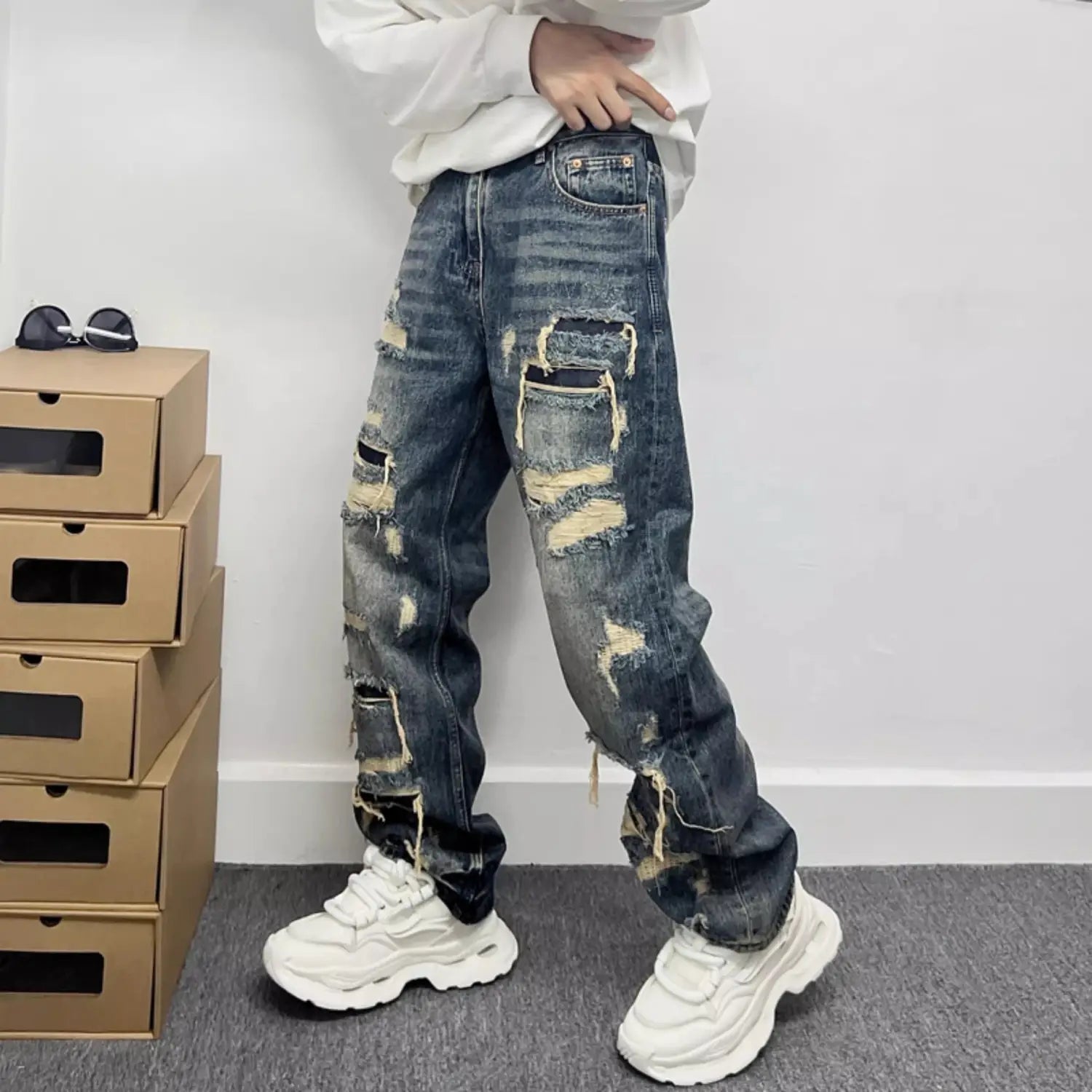Men’s light blue distressed ripped patch denim jeans featuring dark blue material with multiple ripped patches and frayed edges.