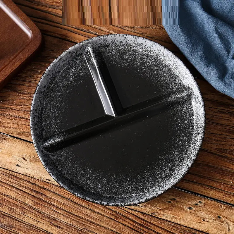 Assiette de dîner divisée en céramique noire à finition mate à mouchetures, avec trois compartiments distincts pour des repas portionnés