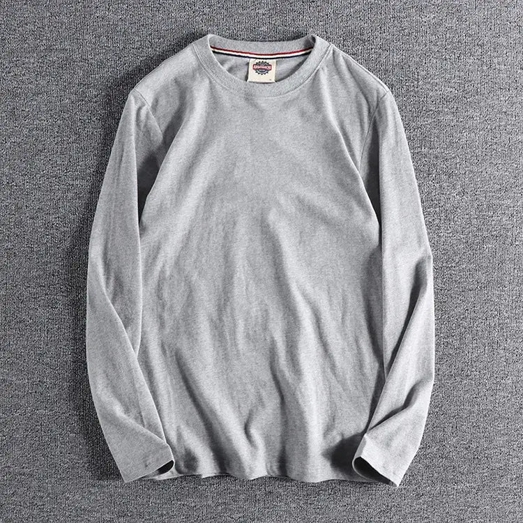 Camiseta de color liso lavado gris de manga larga con una tela sutilmente texturizada y una pequeña etiqueta de marca en el cuello.