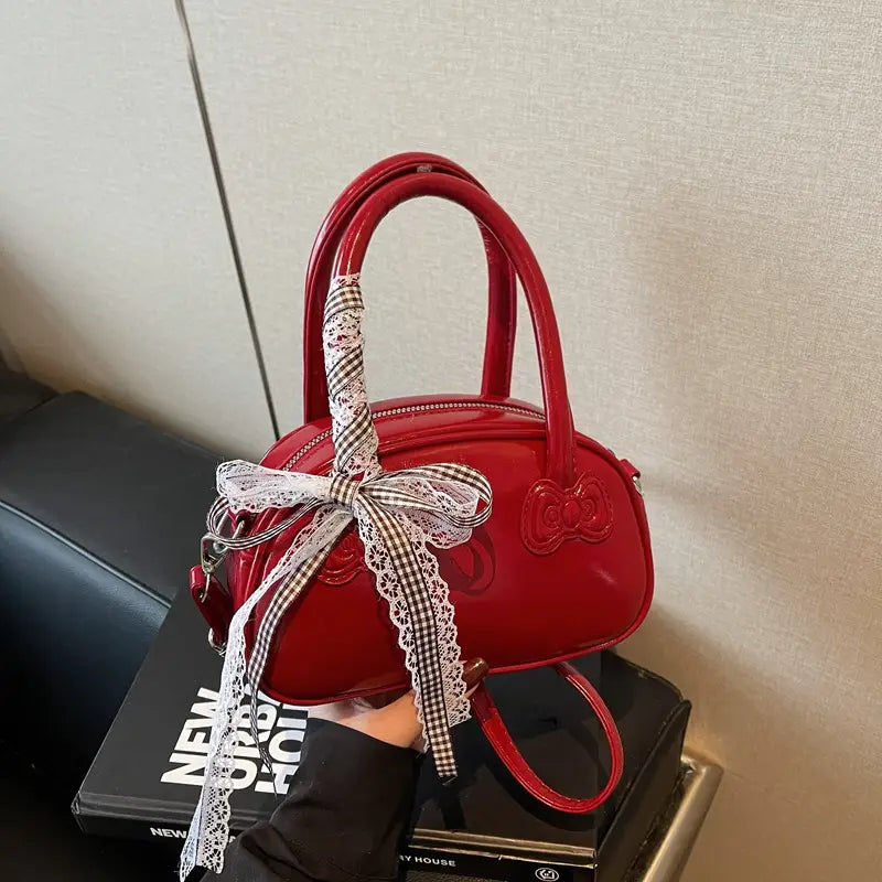 Hello Kitty glossy lace bow crossbody bag featuring a glossy red handbag with a black and white gingham ribbon bow edged in lace and a matching embroidered bow on the front.