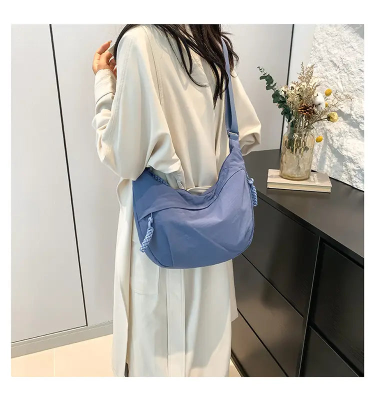 A soft blue lightweight nylon crossbody bag with braided tassels on the side designed as a large capacity hobo shoulder bag.