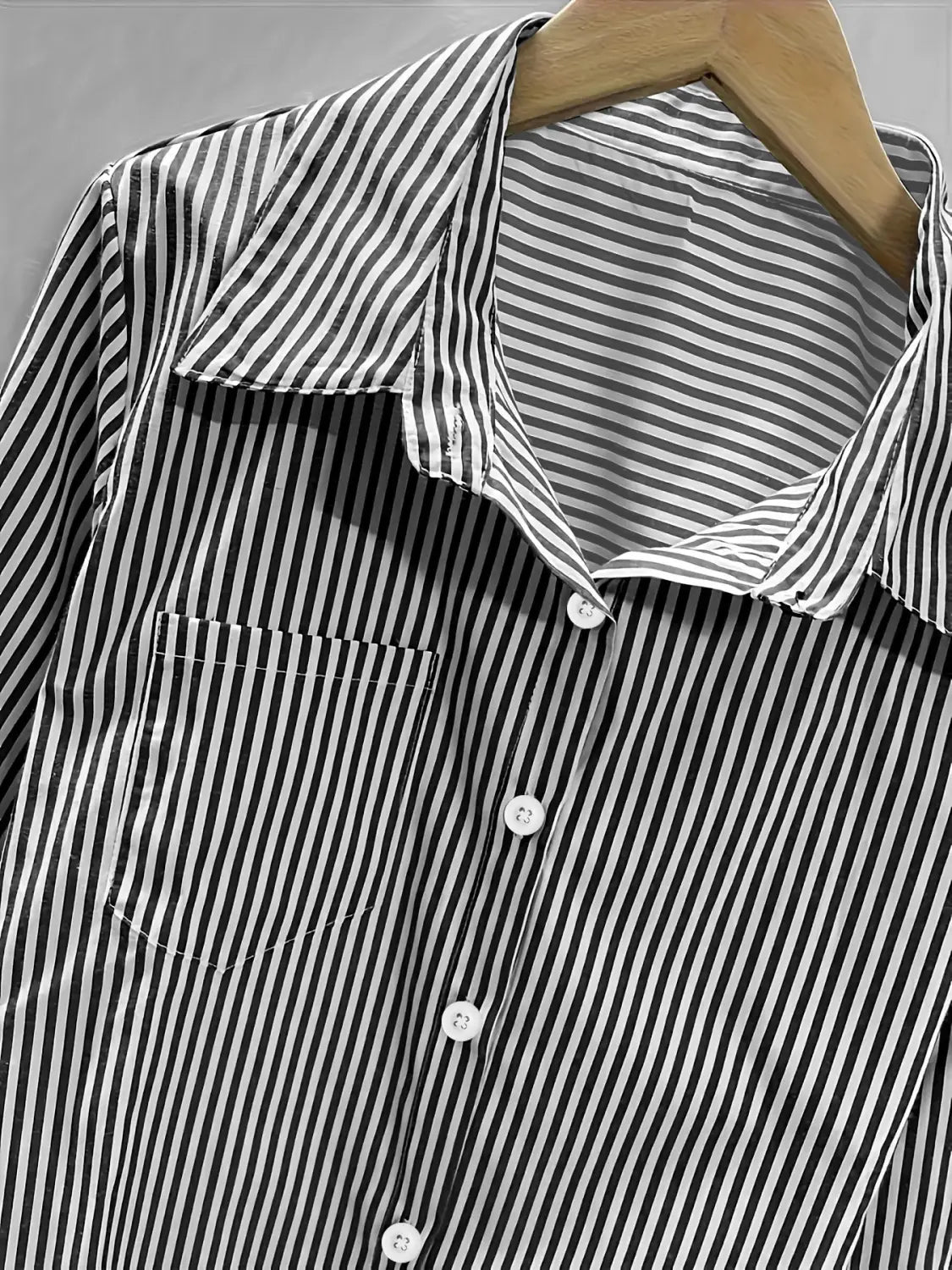 Chemise boutonnée à rayures verticales noir et blanc à manches longues, col classique, boutons assortis et poche poitrine, adaptée à un usage décontracté.