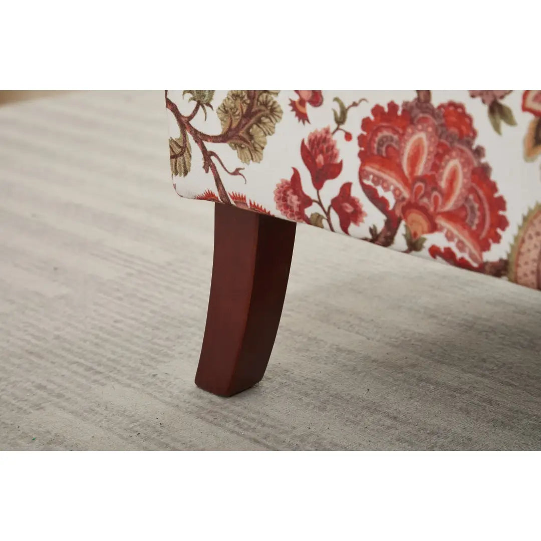 Una pata de madera oscuro color marrón rojizo, con un diseño elegante y curvado, que sostiene la silla tipo ala con respaldo capitoné floral con la tapicería de patas de madera retro