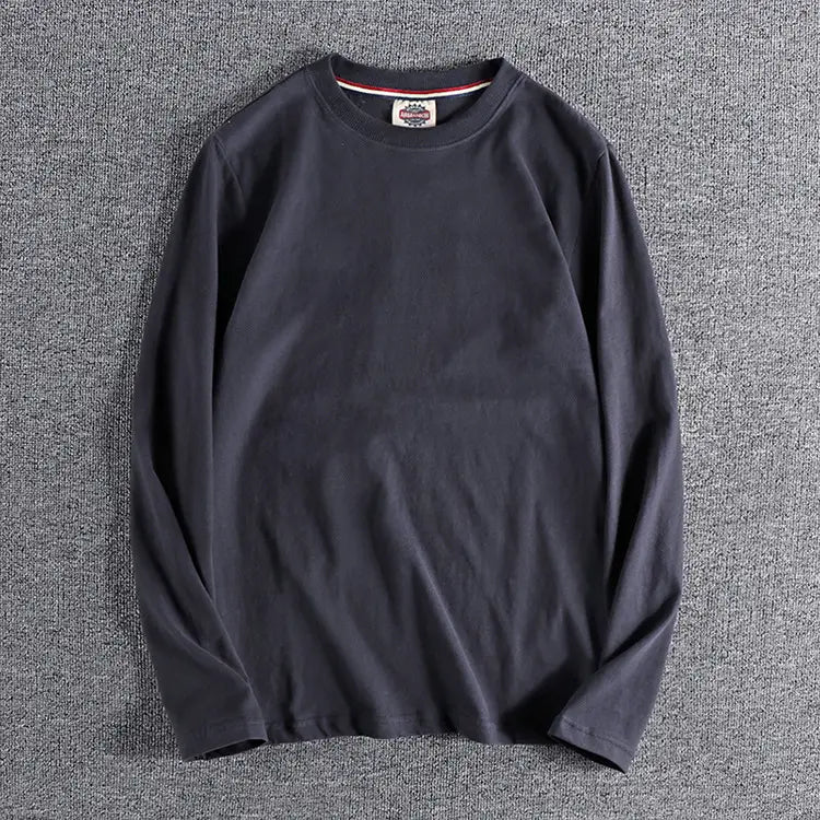 Camiseta tipo jersey de color liso lavado negra de manga larga con cuello redondo y un sutil ribete rojo y blanco a lo largo del cuello.