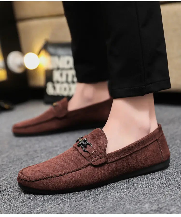 Mocassins à enfiler en daim marron pour homme avec mors de cheval, comportant un détail de boucle métallique noire.