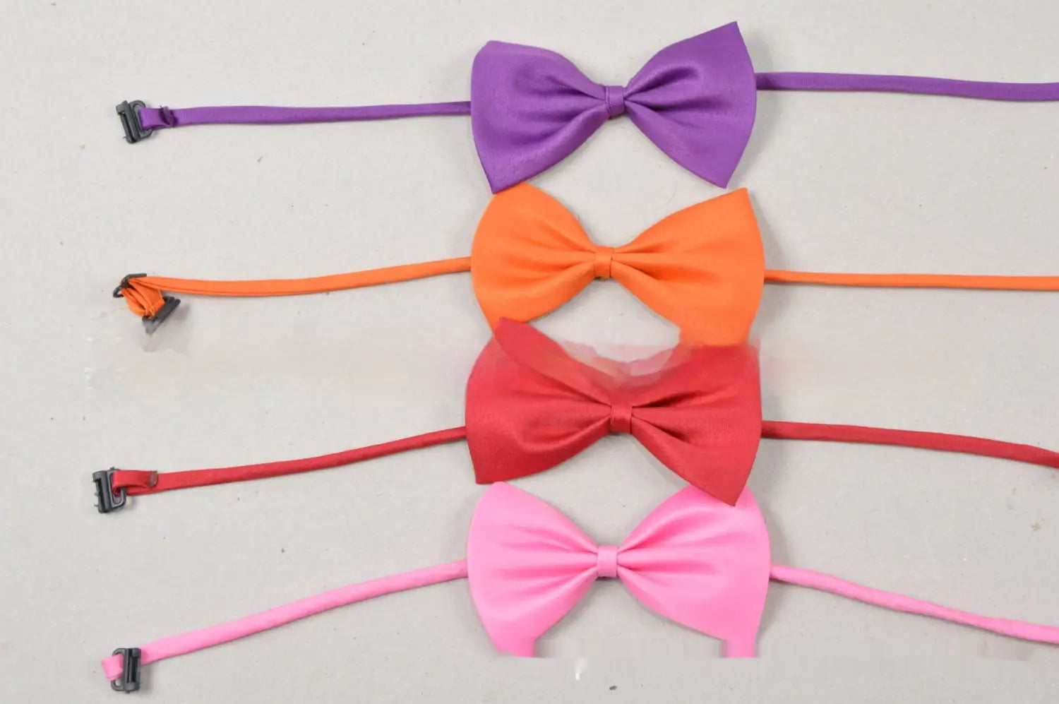 Un conjunto de cuatro lazos satinados de colores unidos a bandas elásticas a juego con clips de plástico, diseñados como collares para mascotas de color sólido ajustables.