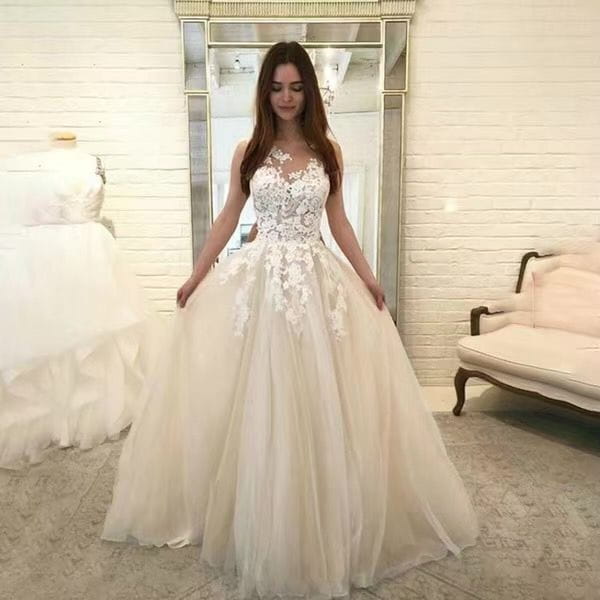 A woman wears an elegant ivory sleeveless lace and tulle floral wedding gown with intricate lace appliqués and a flowing tulle skirt.
