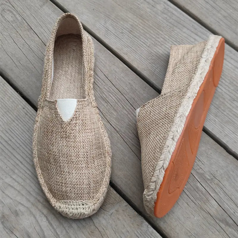 Beige men’s canvas espadrille slip-on summer shoes with a woven jute upper, white triangular patch at the vamp, and an orange rubber sole.
