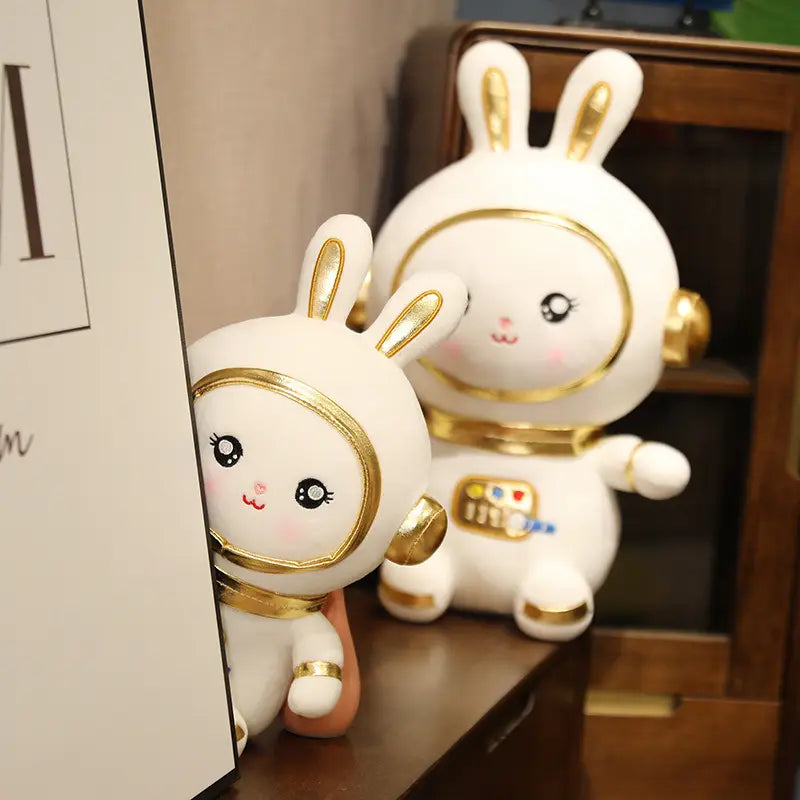 宇宙ウサギをモチーフにした、金色で縁取られたヘルメットとアクセントが特徴のかわいらしい白い宇宙飛行士のウサギぬいぐるみ(詰め物)です。