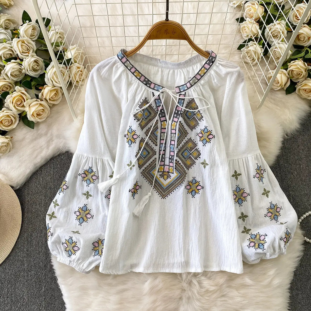 White embroidered lantern sleeve blouse with colorful geometric patterns and a tie-front neckline made of lightweight fabric.