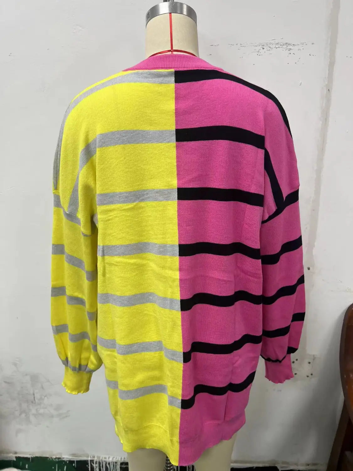 Women’s oversized split color striped knit sweater featuring a vibrant two-tone knit cardigan with bold yellow and pink halves accented by contrasting horizontal gray and black stripes.