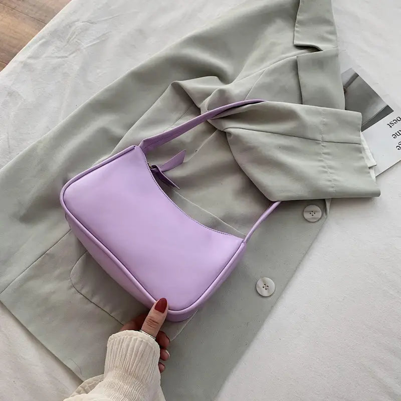 Eine sanfte lavendelfarbene minimalistische Umhängetasche aus Kunstleder mit gebogenem Unterarmgriff, mit elegantem glattem Design.
