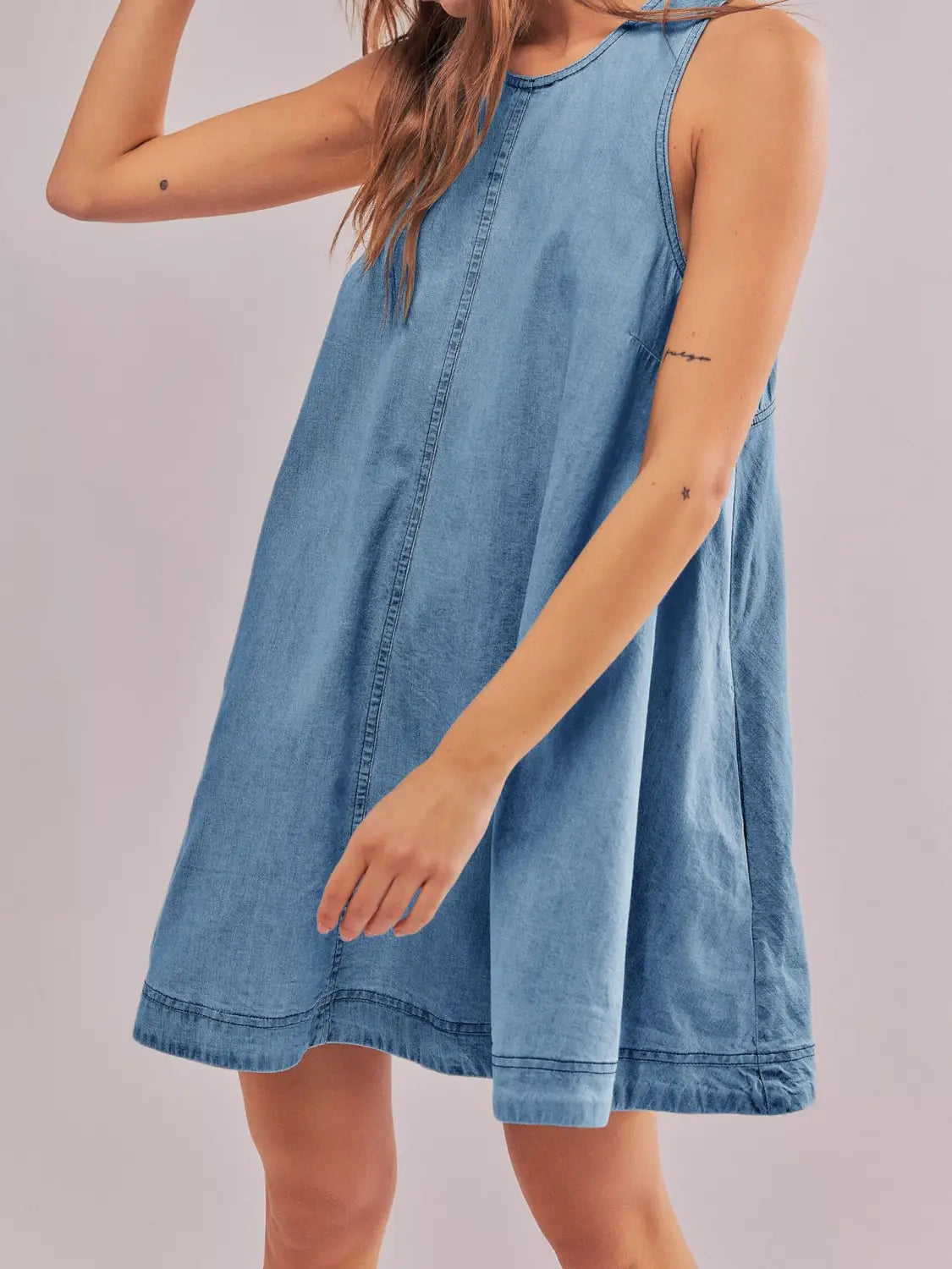 Ein ärmelloses Jeans-Minikleid in hellem Wasch, mit entspannter Passform, hinten offenes Schleifen-Detail und sichtbarer Ziernähte entlang der Nähte.
