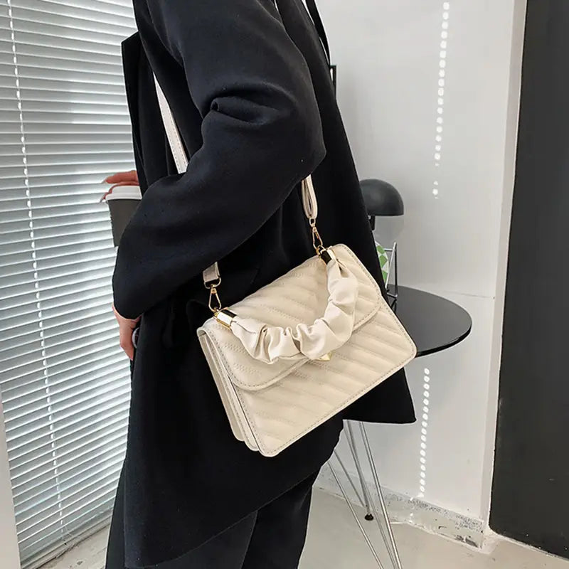 Cream-colored quilted crossbody bag with ruched fabric handle and gold-tone heart clasp hardware.