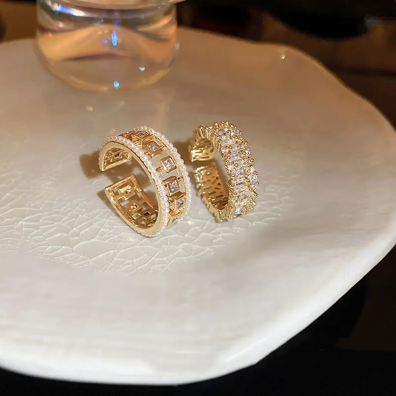 Two gold-toned open hoop earrings from the hollowed square pearl and baguette zircon open ring collection featuring a geometric pattern with clear crystals and a continuous row of rectangular-cut stones.