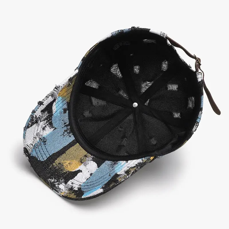 Une casquette de baseball en coton à projections de peinture vieillies, présentant un motif abstrait audacieux en noir, blanc, bleu et jaune.
