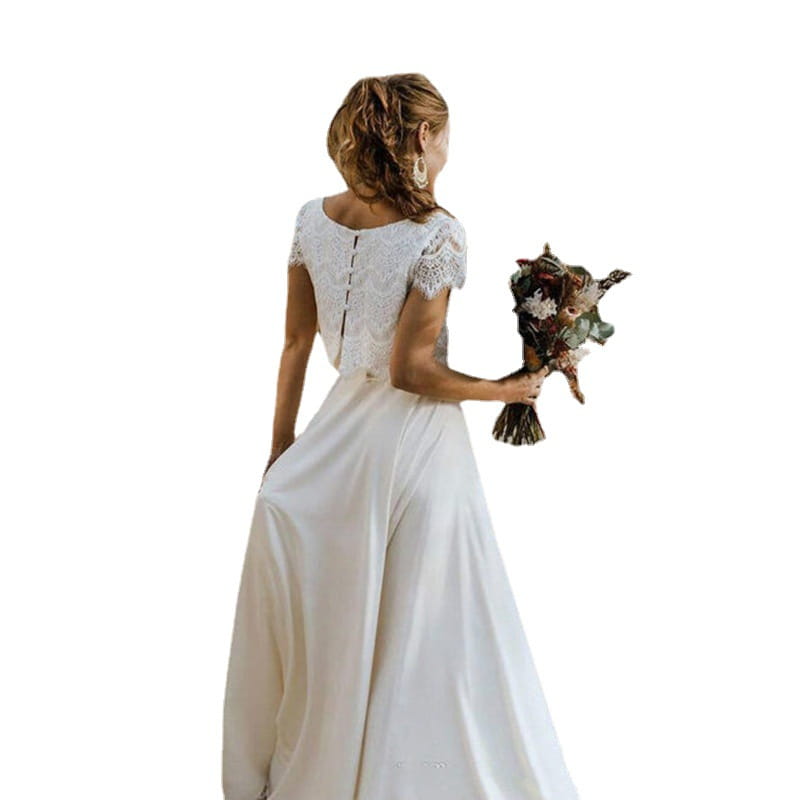 Robe de mariée en dentelle blanche avec manches courtes, décolleté bijou et jupe fluide, destinée à un usage nuptial.