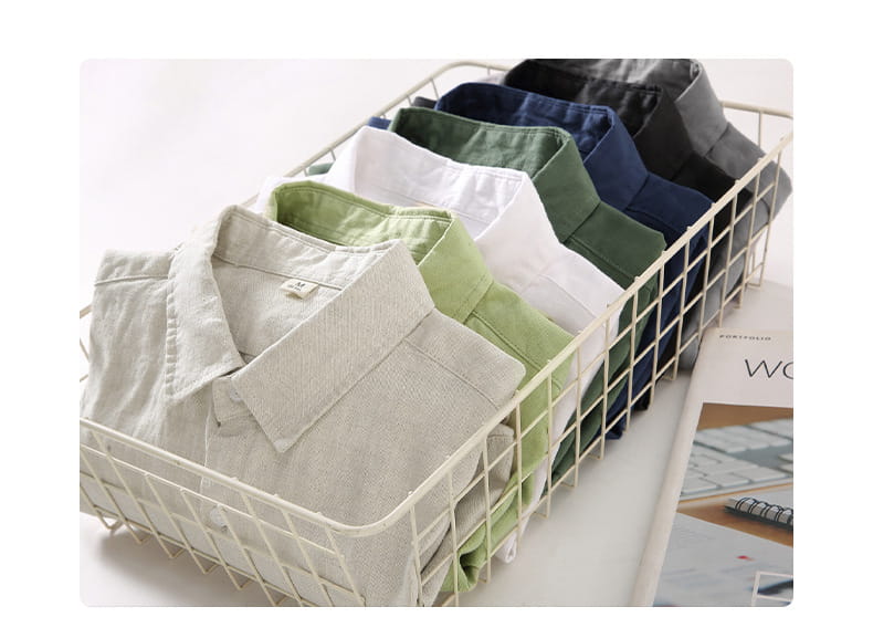 Une collection de chemises boutonnées de protection solaire en lin pour homme, de couleur unie, soigneusement pliées, dans un panier en fil blanc.