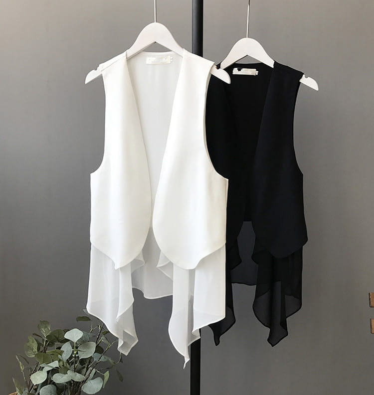 Weiße und schwarze transparente Chiffon-Lagenröcke mit asymmetrischer Passform, auf weißen Bügeln hängend, die leichte ärmellose Oberbekleidung präsentieren