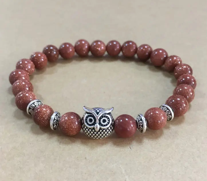 A red sandstone bead bracelet with a silver owl charm and decorative metallic spacers featured in a natural lapis lazuli and lava stone owl charm bracelet.