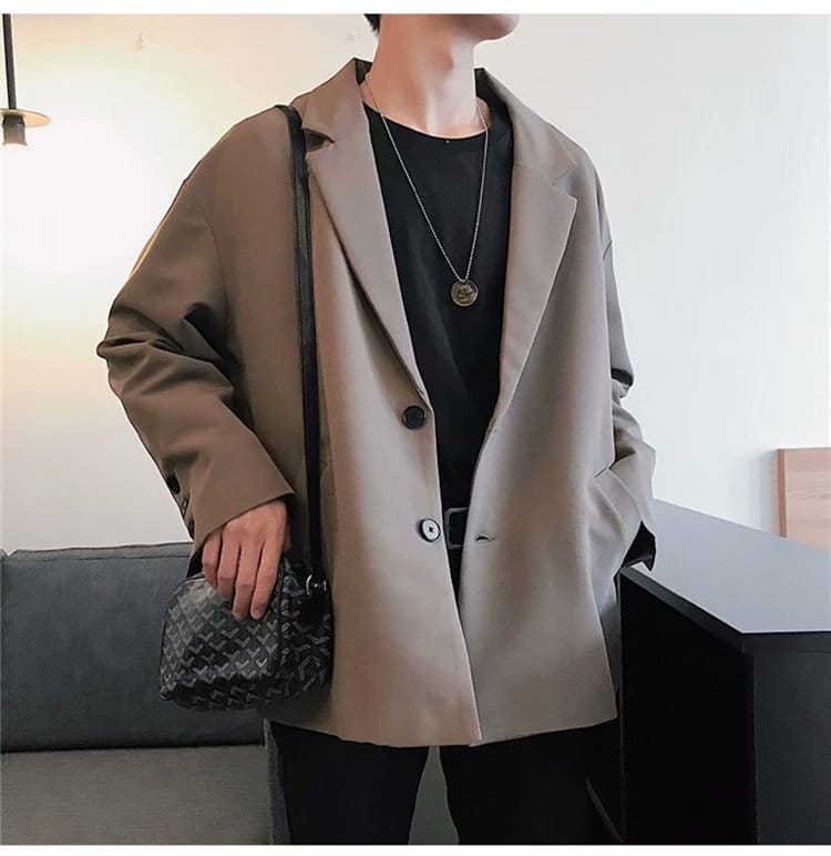 Black and gray patterned crossbody bag with a textured woven design paired with a mens loose casual thin suit jacket.