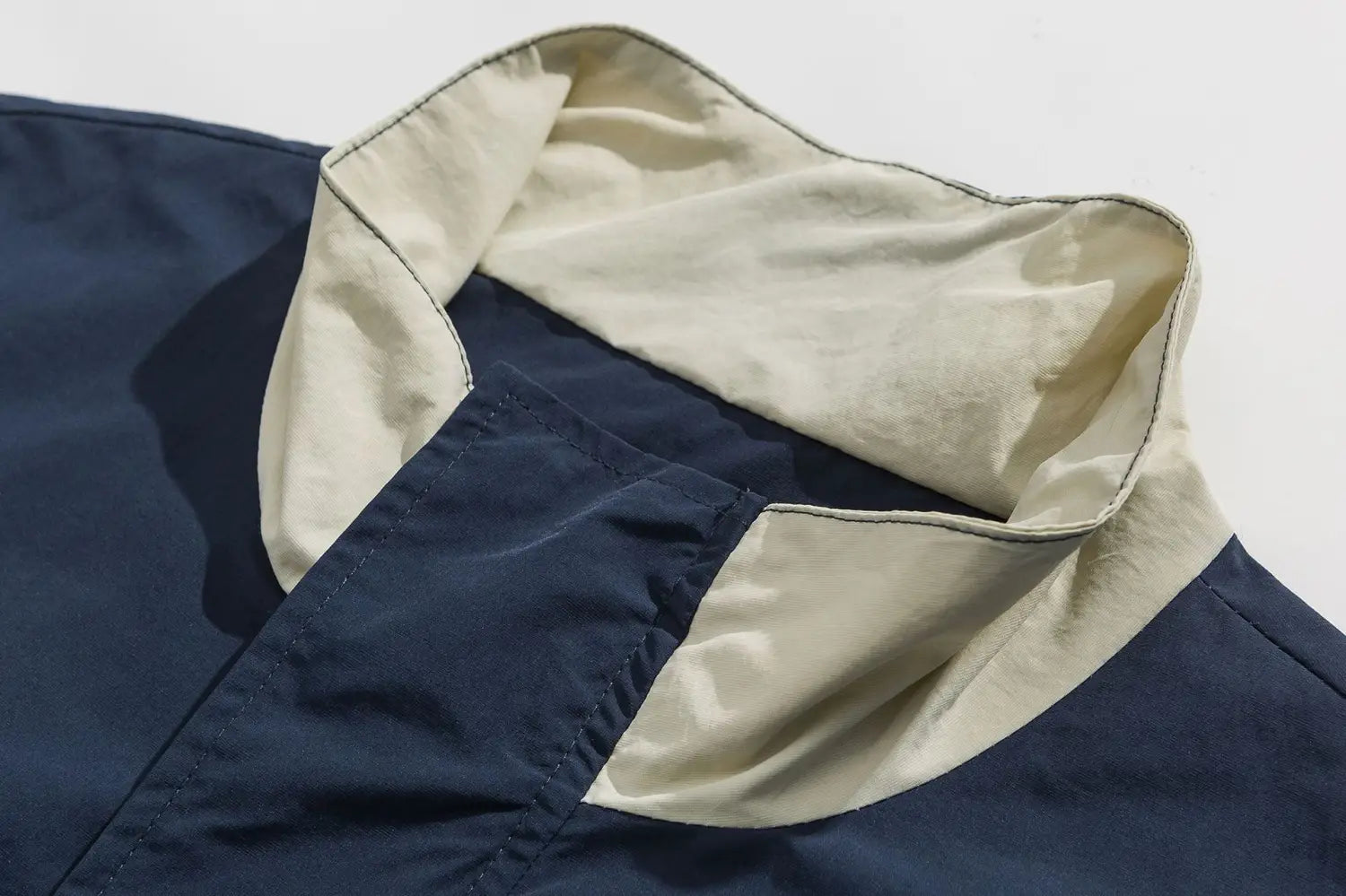 Col bicolore bleu marine et beige à deux tons, avec des coutures contrastantes sur une veste coupe-vent ample à blocs de couleurs brodés.
