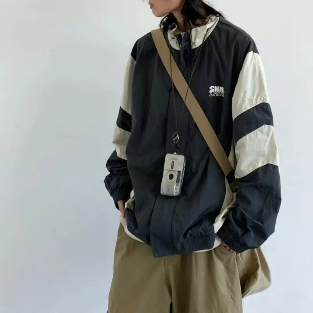 Veste coupe-vent ample à blocs de couleurs brodés bicolores noir et crème, avec de larges rayures horizontales sur les manches.