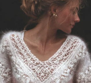 Un suéter de encaje de punto delicado en blanco con degradado rosa suave y escote en V, con detalles de encaje intrincados alrededor del escote y los hombros.