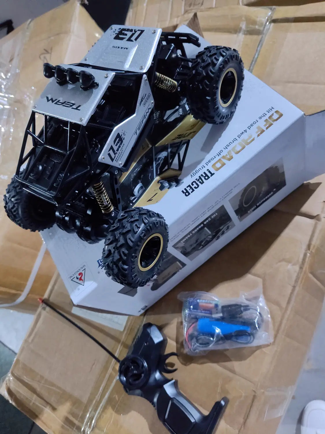 Camion teledirigido RC todoterreno 4WD de alta velocidad en negro y plata, tipo crawler, con suspensión con detalles dorados y neumáticos resistentes para la conducción en terrenos difíciles.