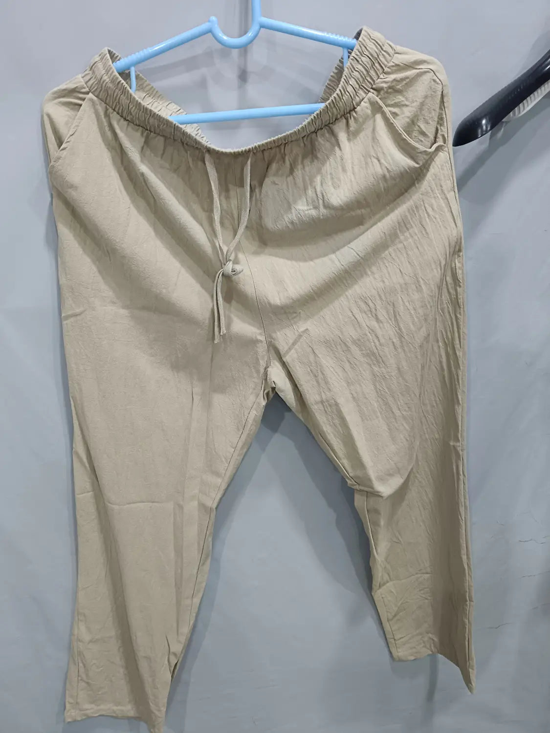 Beige cotton drawstring pants with an elastic waistband and tapered legs for men’s casual linen joggers.