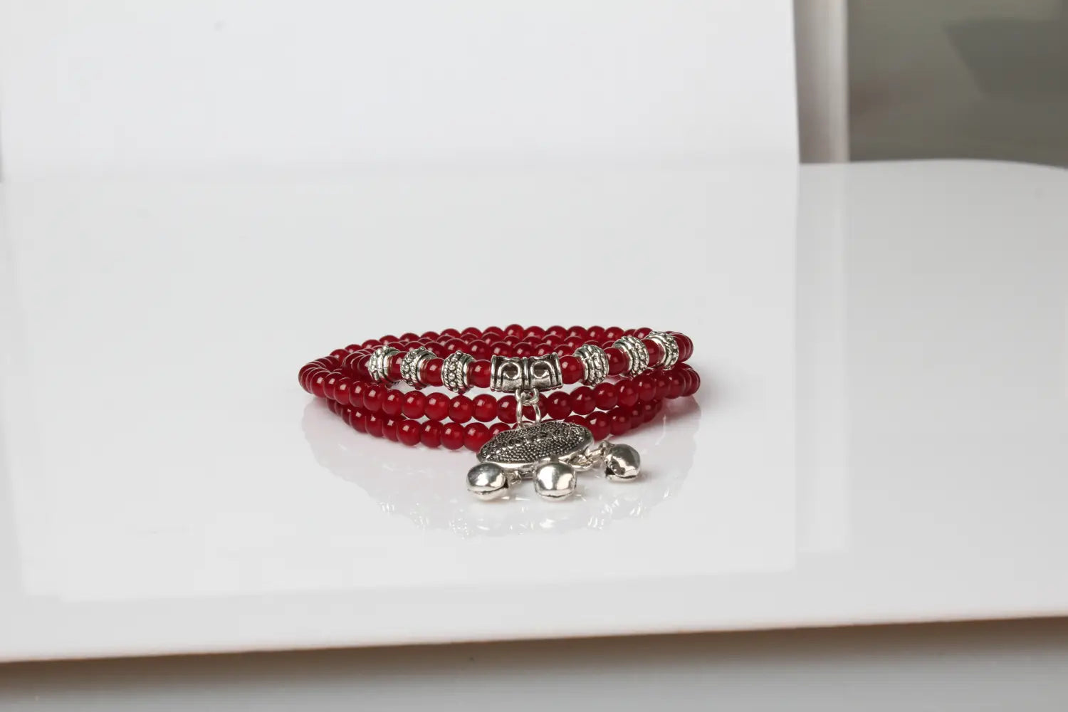 Red agate good luck bracelet featuring red beads with silver-toned metal accents and a dangling engraved turtle protect charm.