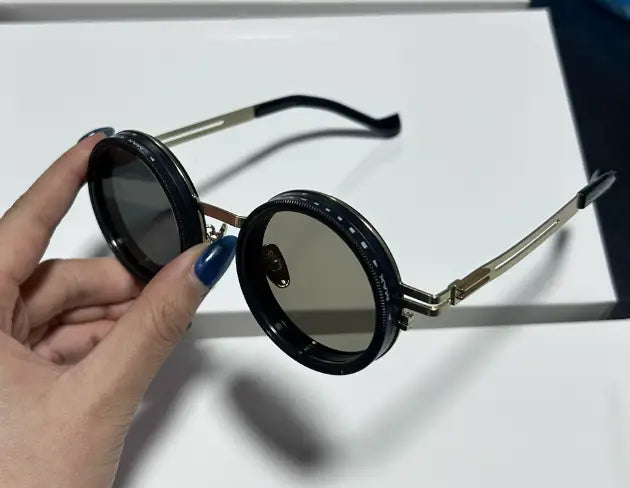 Lunettes de soleil rondes unisexes résistantes aux UV, avec monture noire ronde, branches en métal à finition dorée et verres gris foncé.