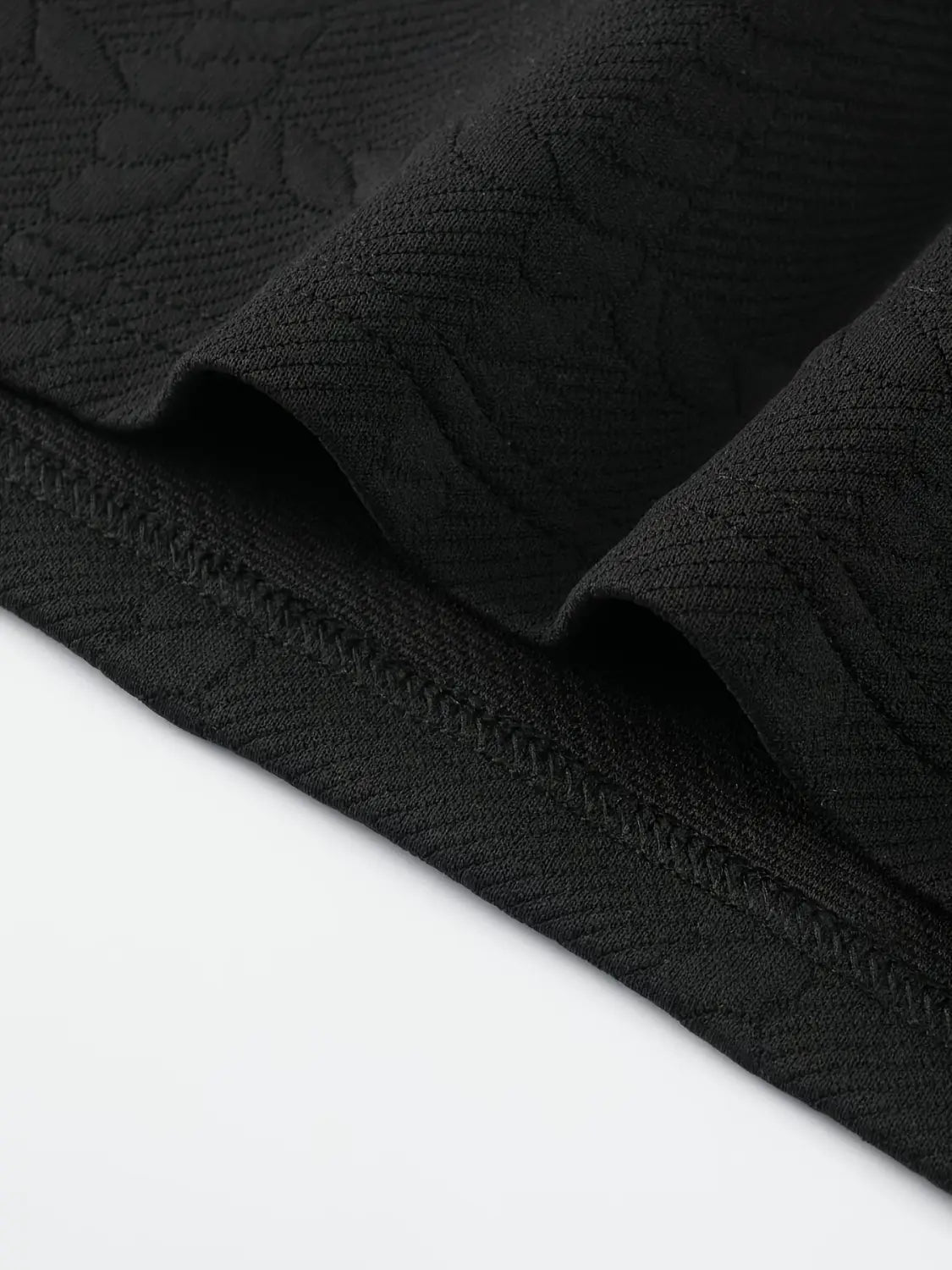 Camisa tipo polo de manga larga negra con textura que presenta un sutil patrón bordado y una costura esmerada a lo largo del bajo.