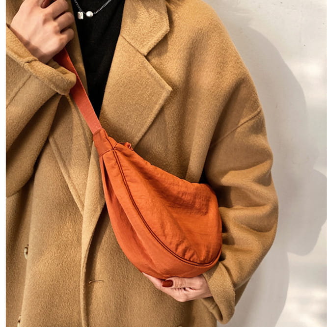 Orange nylon dumpling messenger bag with curved crossbody strap and matching strap.