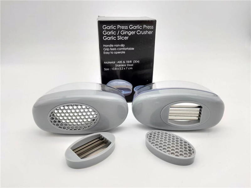 Presse-ail en plastique gris avec grille en nid d’abeille et lames en acier inoxydable, dans un étui gris conçu pour un écrasement efficace de l’ail.