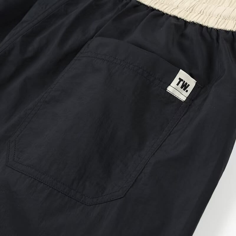 Shorts en nylon décontractés pour hommes, coupe droite, noirs, avec une ceinture élastique beige et une petite étiquette blanche sur la poche avant.